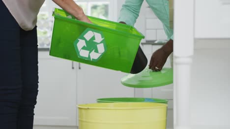 Senior-diverse-couple-wearing-shirts-and-segregating-waste-in-kitchen