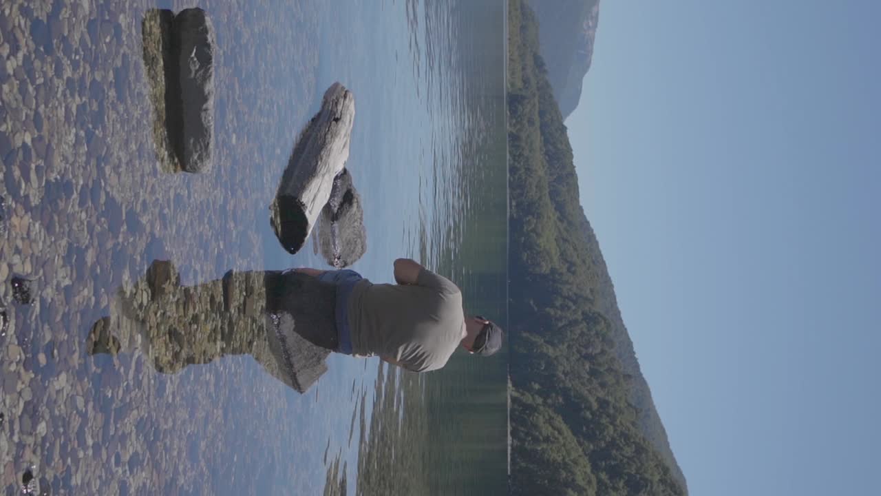 un hombre con una gorra de béisbol relajándose en un lago con aguas claras con bosques y colinas en el fondo