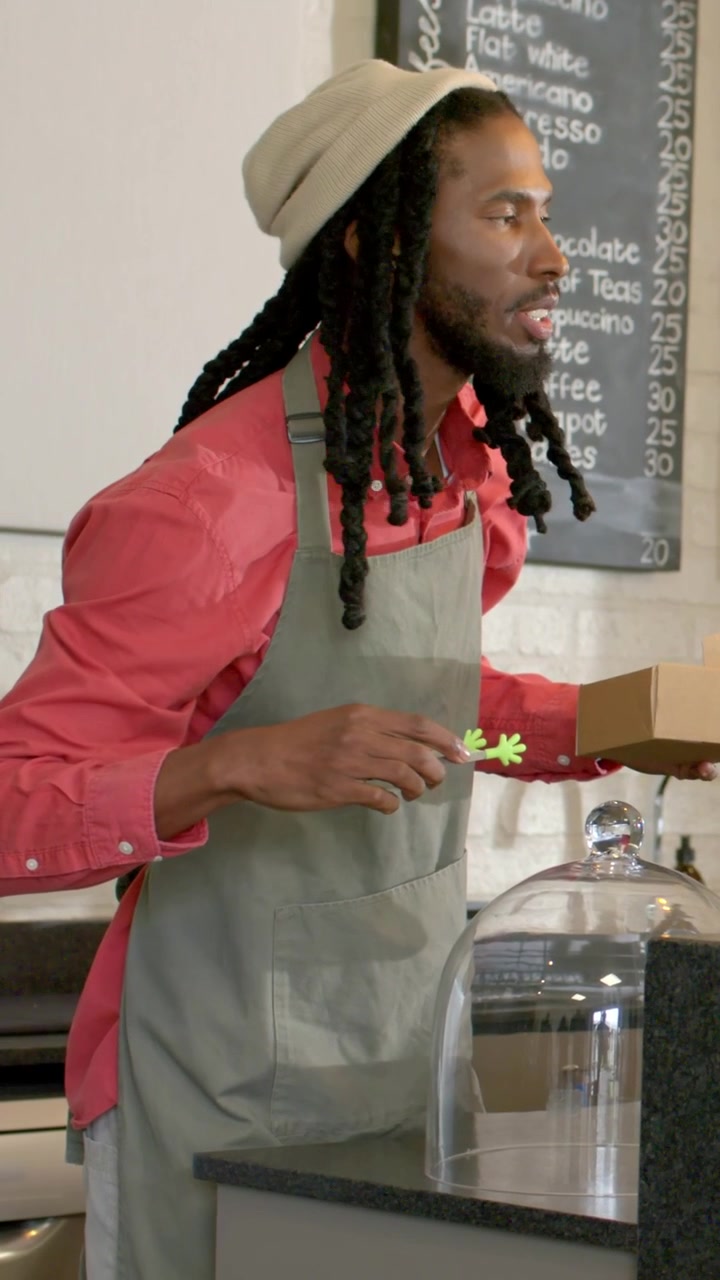 Vertical video: Reaching counter server wearing beanie apron opening box for order using green pick