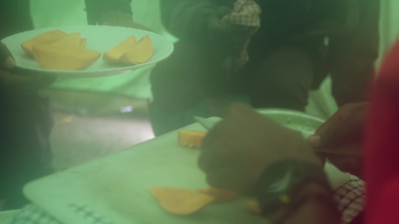 A cook with an assistant preparing lunch cutting mangoes
