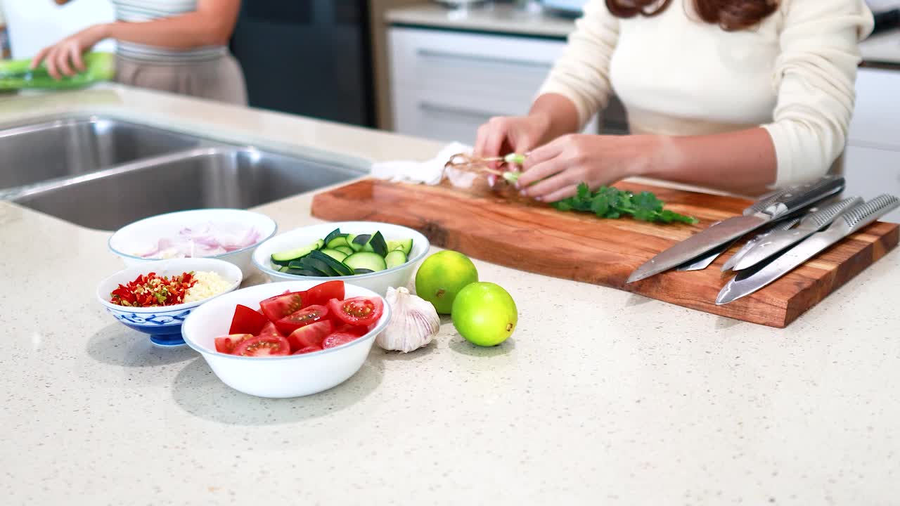 Two people prepare fresh vegetables and herbs on a kitchen counter with bright lighting and a clean, modern aesthetic