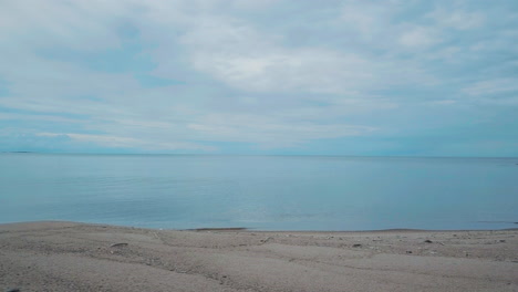 calm sandy beach and coastline on cloudy day, low angle panning shot