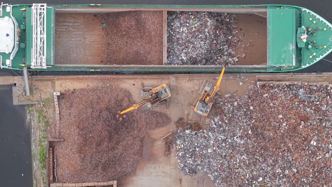 Excavators Loading Shredded Metal Into Cargo Ship Docked At Scrap Yard In Port Of Limerick, Ireland aerial topdown shot