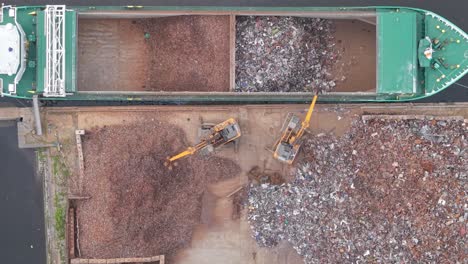 excavators loading shredded metal into cargo ship docked at scrap yard in port of limerick, ireland aerial topdown shot