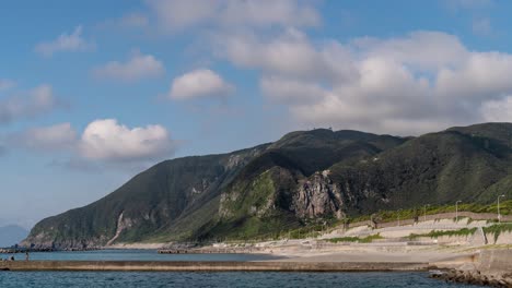 Fast-moving-cloud-time-lapse-casting-shadow-on-green-cliffs-with-ocean-and-beach-in-foreground