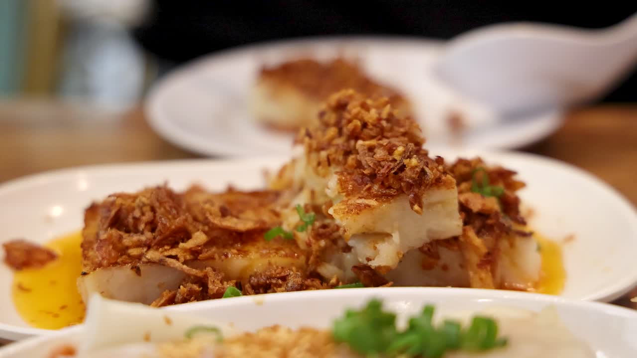 A close-up sequence shows chopsticks picking up a piece of fried turnip cake topped with crispy shallots in a warmly lit Singapore restaurant