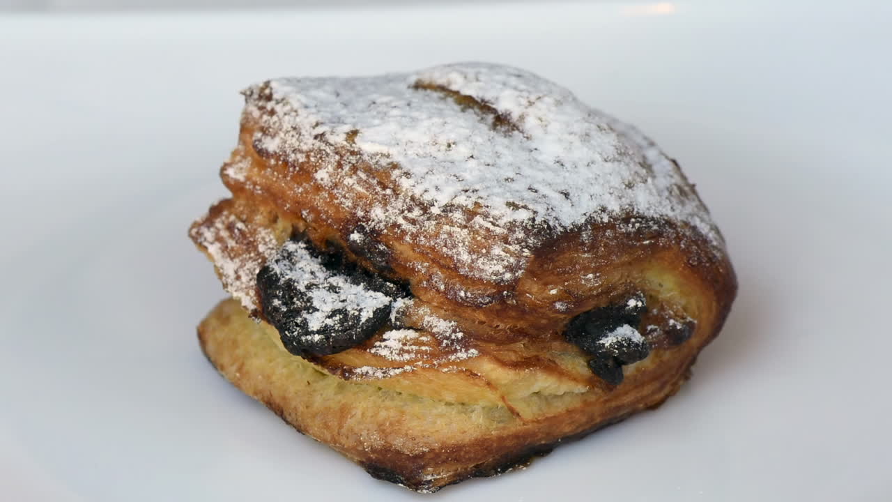 Close up of spinning a puff pastry with jam and powdered sugar on a white plate