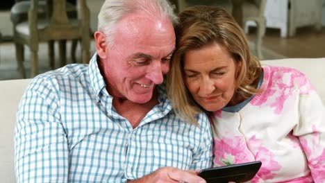 smiling senior couple reviewing captured photos on mobile phone in living room