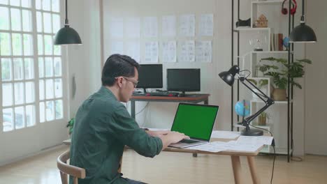 asian man works on laptop computer with mock up green screen display and storyboard. video editing, comics compilation, application ui or game plot