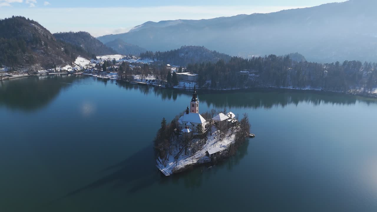 L'iconica Isola di Bled nel lago glaciale e la riva coperta da neve invernale, ripresa aerea.