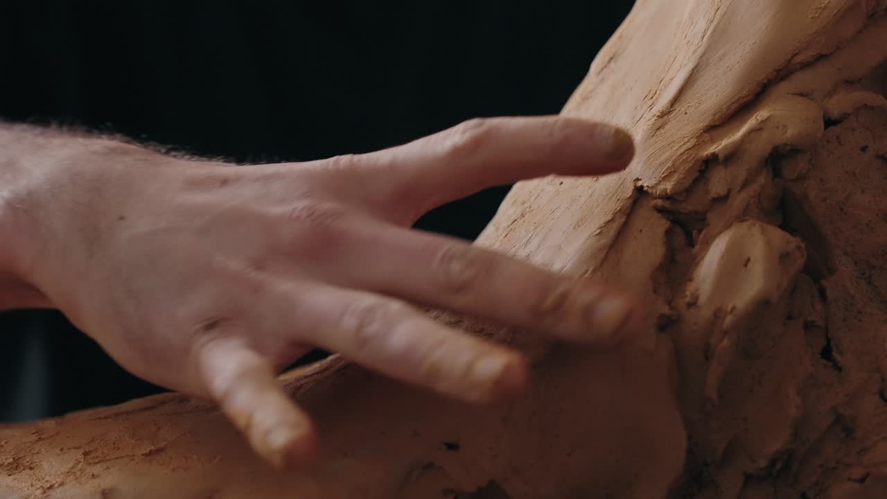 Close up of sculptor’s hand gently smoothing clay surface in a studio environment