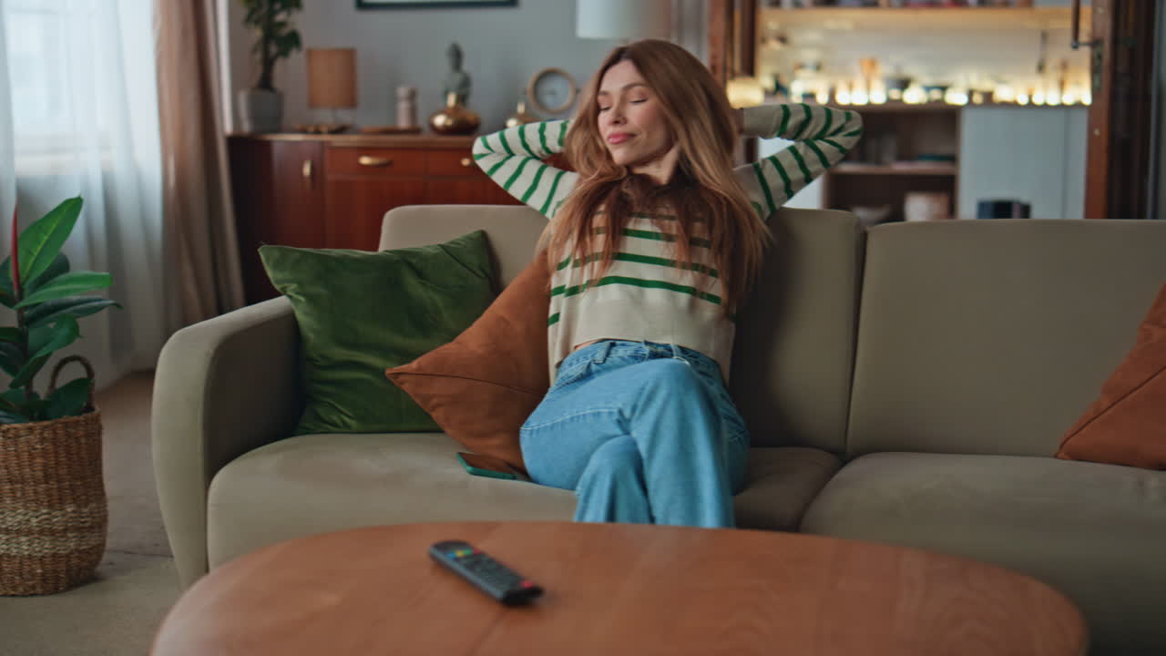 Carefree girl relaxing couch at modern living room. Happy woman taking cellphone