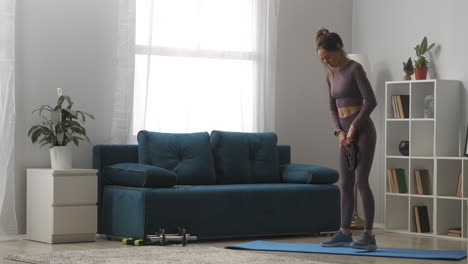 mujer deportiva está viendo en el rastreador de fitness y haciendo sentadillas con peso en el apartamento hogar gadget de actividad de fitness para controlar los parámetros de salud