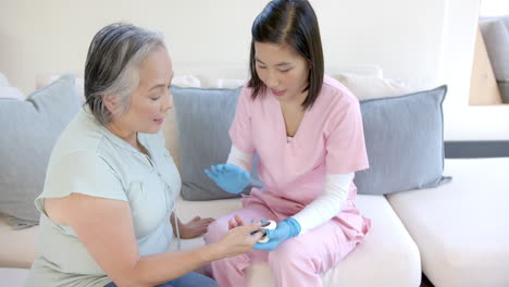 healthcare worker in pink scrubs checking blood sugar level of senior asian woman