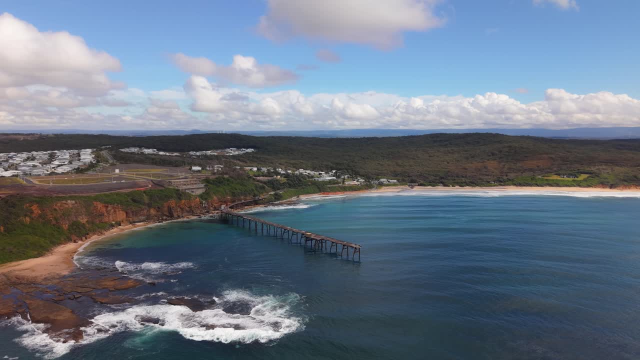 Aerial establishing orbit of rocky coastline and cliff walk jetty structure at Catherine Hill Bay, NSW with ocean waves
