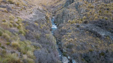 Blue-creek-through-grassy,-rugged-canyon;-aerial-orbit