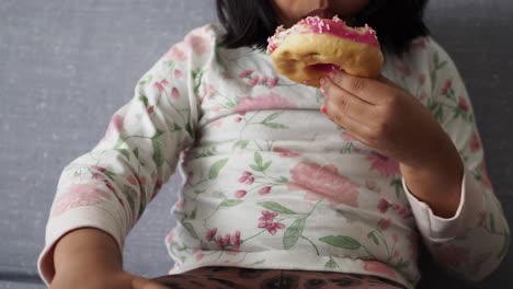 young girl happily eating a pink glazed donut