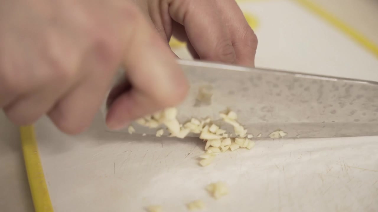 Primo piano di mani che tagliano l'aglio su un tagliere bianco