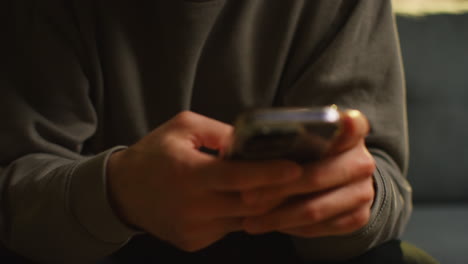 close up of man spending evening at home sitting on sofa wearing wireless headphones streaming music or watching content from mobile phone