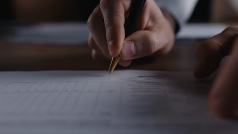 Close-up-of-a-guy-writing-down-a-signature-on-a-piece-of-paper-in-a-document-using-a-black-pen-in-the-office