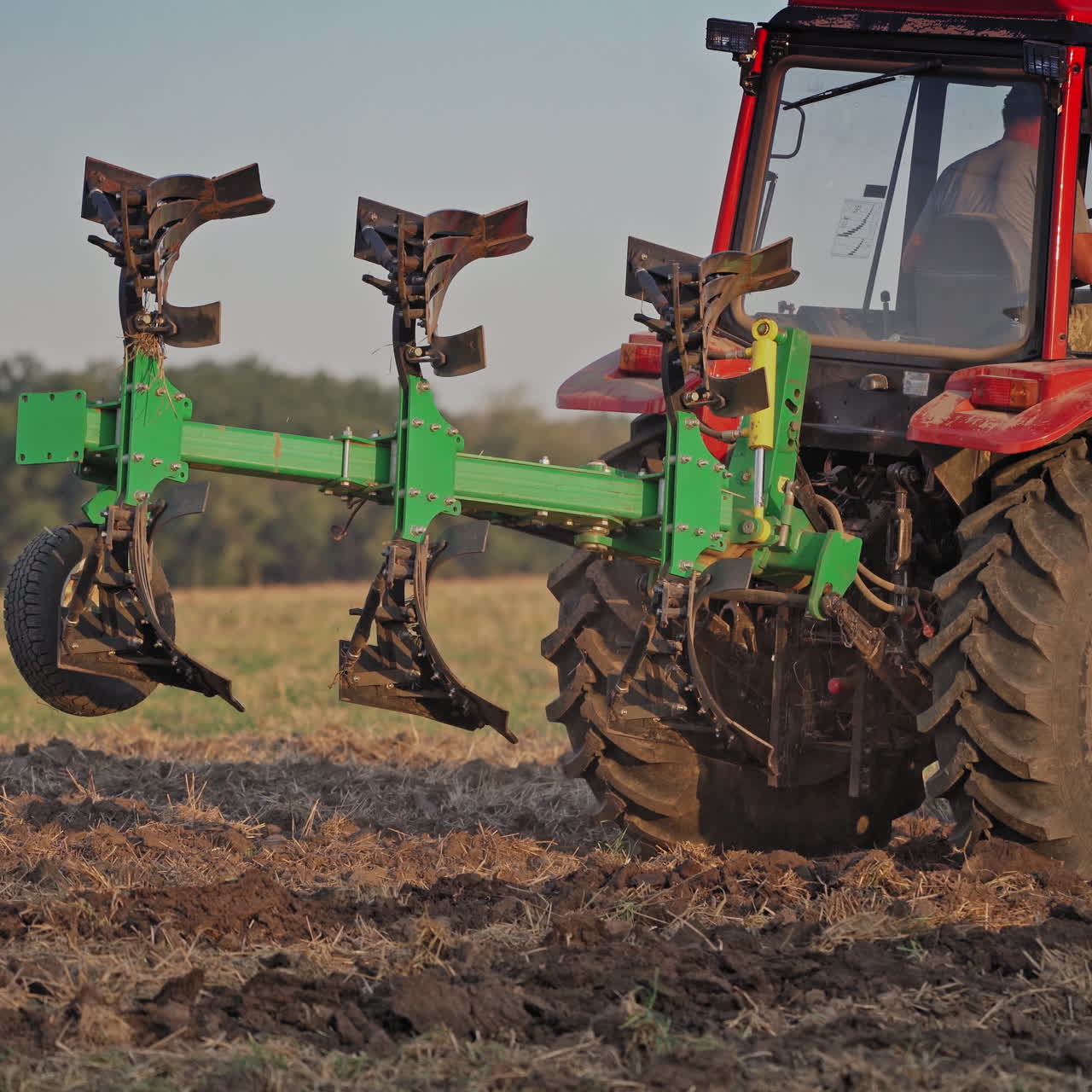 Farmer in tractor customize equipment for cultivating the soil. Close-up view of agricultural tractor in the field at daytime. Seasonal works in rural place.
