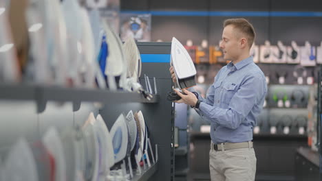 a young handsome man examines the iron in the store to buy a new house. selection of smart tech iron