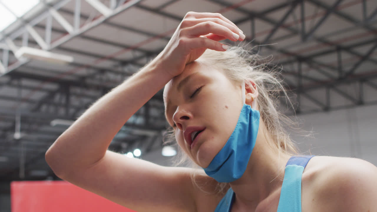 Donna caucasica con mascherina abbassata che si asciuga la fronte in palestra