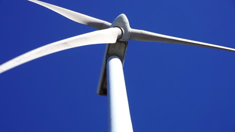 close-up view of a wind turbine's blades spinning against a blue sky background