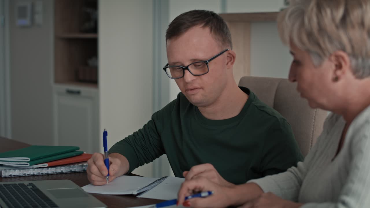 Caucasian man with down syndrome learning with his mum at home