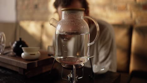 man preparing tea in a glass teapot on a stove