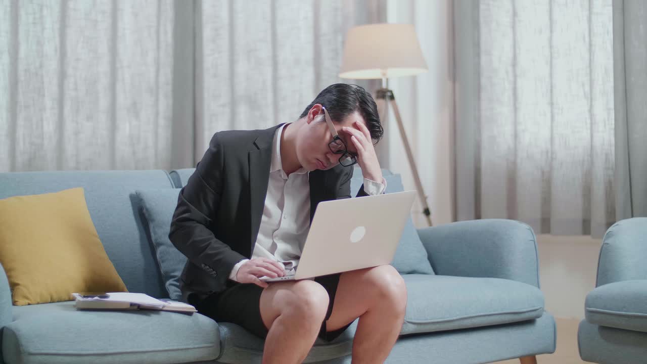 자켓과 쇼트를 입은 아시아 사업가 가 집에서 노트북으로 일하면서 두통을 고 있다