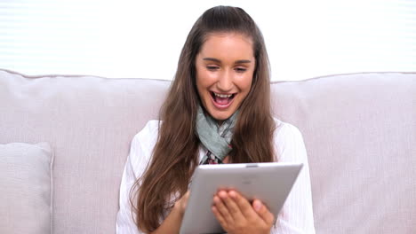 una morena feliz usando una tableta en el sofá
