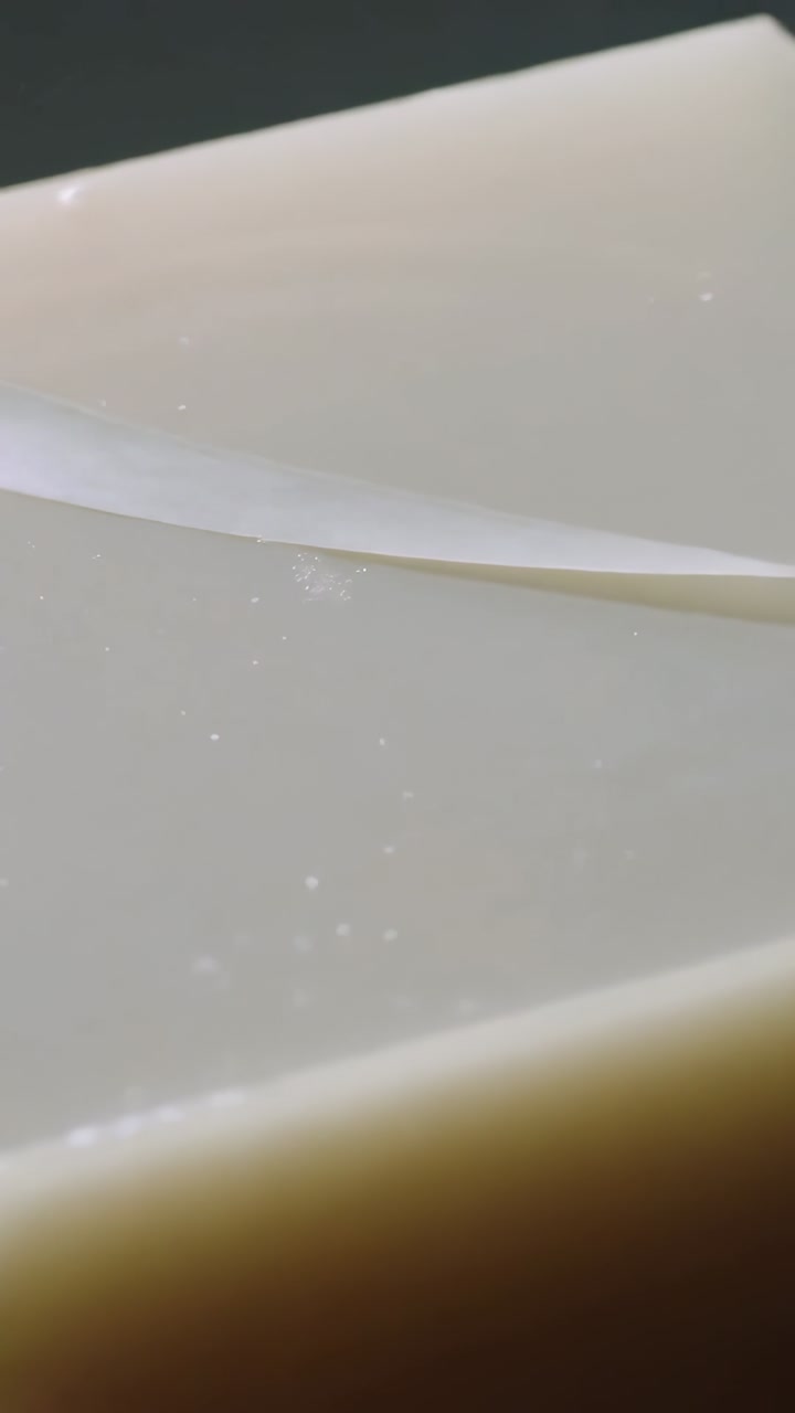 Vertical video: Unrolling ribbon sliding across cream block in studio, revealing liquid ripples
