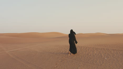 Rückansicht-Einer-Muslimischen-Frau-Mit-Hijab,-Die-Barfuß-In-Einer-Windigen-Wüste-Läuft