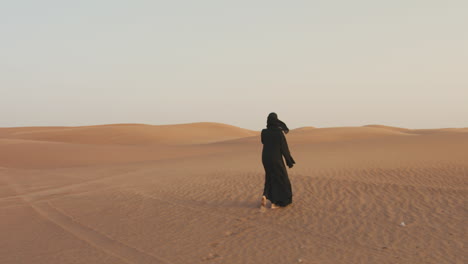 vista trasera de una mujer musulmana con hijab caminando descalza en un desierto ventoso