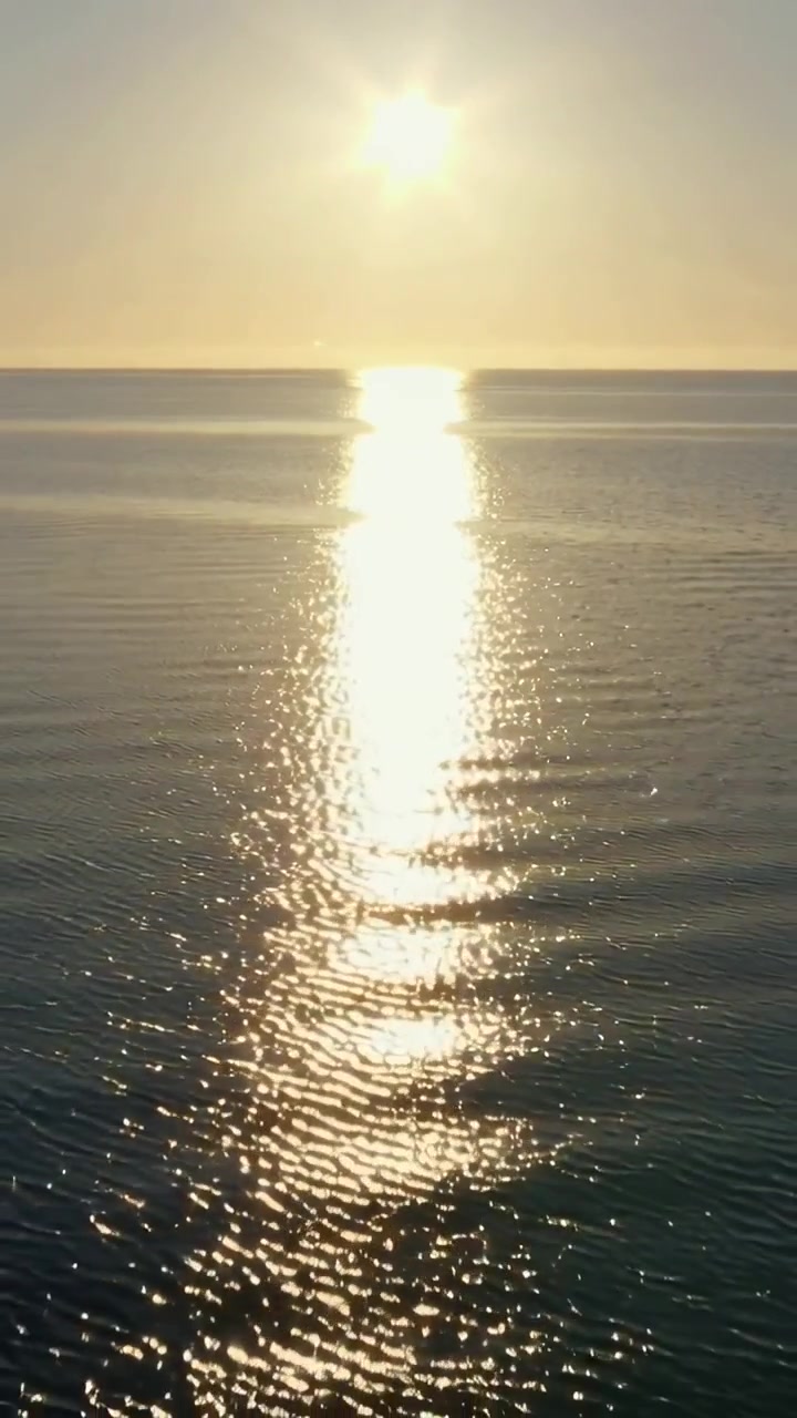 Vertical video: Shimmering sun vertical light beam across sea at horizon, wind rippling glare