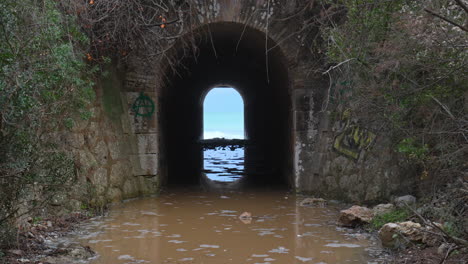 a tunnel leads towards a wild sea, where incoming waves create a rippling effect