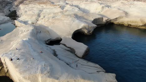 Drohnenansicht-In-Griechenland,-Die-Bei-Sonnenaufgang-über-Einem-Mondförmigen-Weißen-Felsengebiet-Auf-Der-Insel-Milos-Neben-Dem-Dunkelblauen-Meer-Fliegt