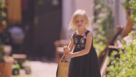 a young happy girl with a gift bag in her hands runs towards the camera, her blonde hair flutters in the wind