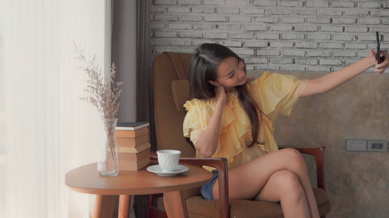 Pretty young Asian female takes selfie on couch, brick background wall
