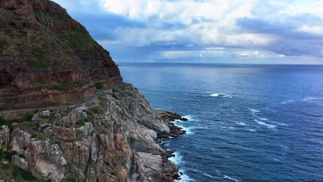 chapman peak drive south africa sunset drive aerial cinematic drone hout bay marina cape town cliffside edge good hope table mountain waves crashing rugged coast aqua deep blue water green forward pan