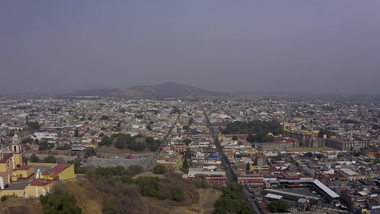 An aerial drone shot captures the iconic Santuario de Nuestra Señora de los Remedios (Church of Our Lady of Remedies) perched atop the Great Pyramid of Cholula in Puebla, Mexico
