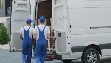 two young workers of removal company are loading boxes and furniture into a minibus