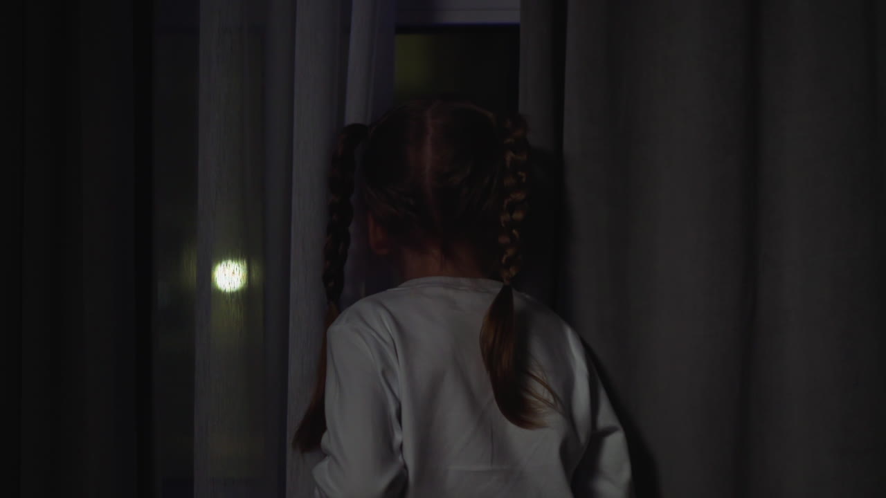 Child looks out of window attracted by blinking flashlights