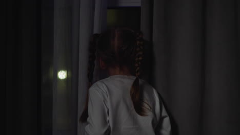 child looks out of window attracted by blinking flashlights