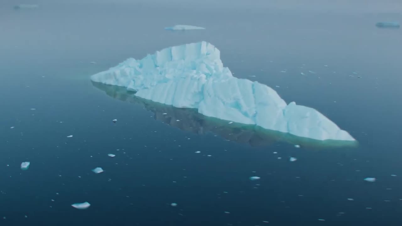 드론 카메라가 그 주위를 날아다니며 더 작은 얼음 조각을 드러내는 동안 북극 해양 해수면에 있는  얼음산의 드론 영상