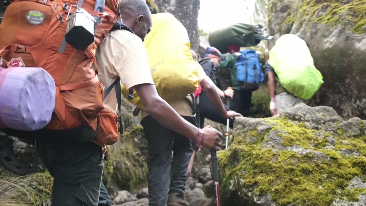 A man with a large backpack and trekking poles walks along the trail