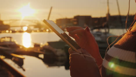 manos de una mujer con un teléfono inteligente en el fondo de un muelle con yates al atardecer 4k video