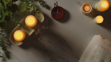 overhead view looking down on still life of lit candles and incense stick with green plant and towels as part of spa day decor