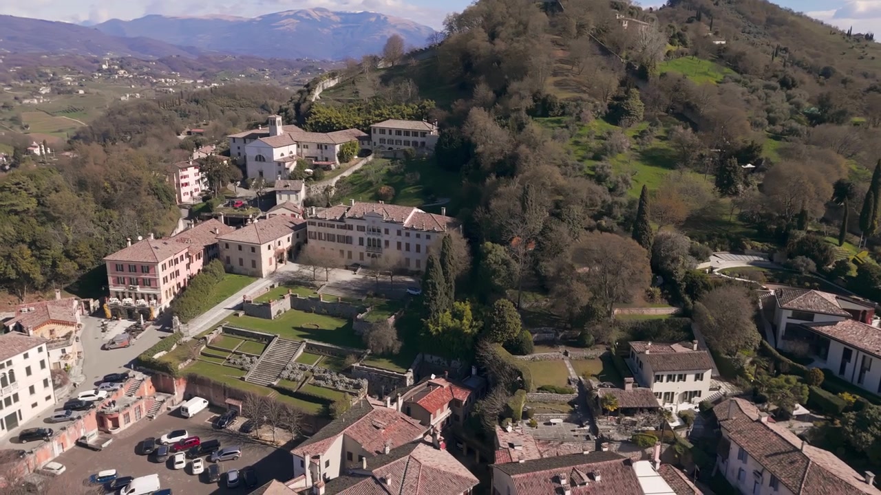 Vista aerea che sorvola una cittadina collinare con edifici storici e rovine di castelli visibili